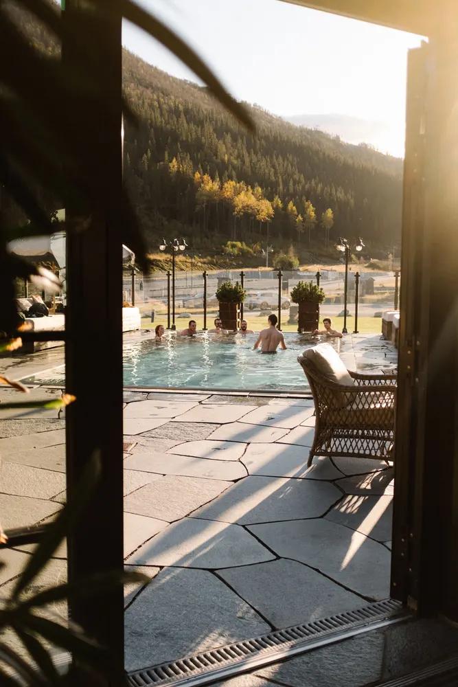 Utendørsbassenget med badegjester og fjellsiden i kveldssol