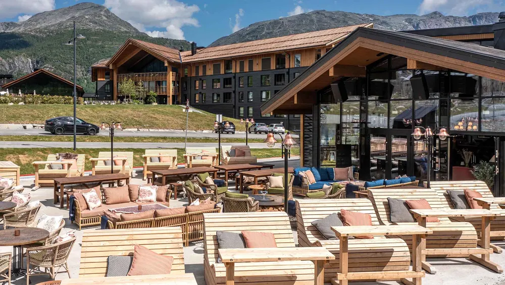 Stor solterrasse med solsenger og sittegrupper foran Fýri Resort, med fjellpanorama i bakgrunnen