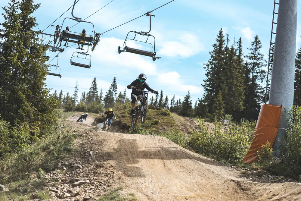 Terrengsyklist svever over et hopp i Hafjell Bike Park med stolheisen over seg