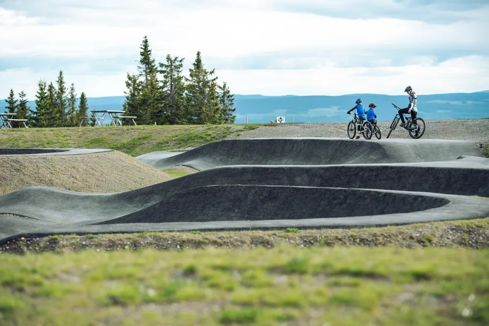 Tre syklister på pumptracken på toppen av Hafjell med fjellutsikt i bakgrunnen